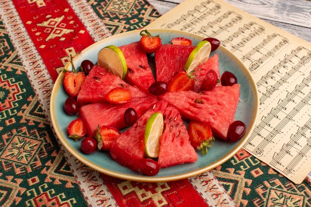 sliced watermelon with strawberries and dogwoods inside green plate on grey