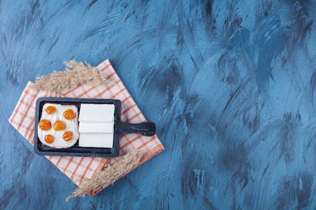 Sliced white cheese and bread with cream and jam on cutting board. 