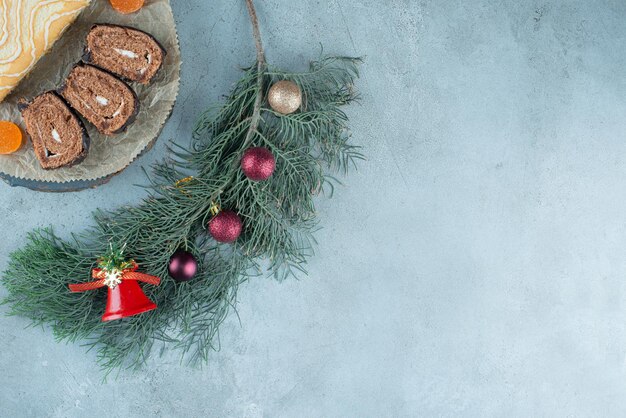 Sliced and whole cake roll on a platter with a decorated pine branch on marble.