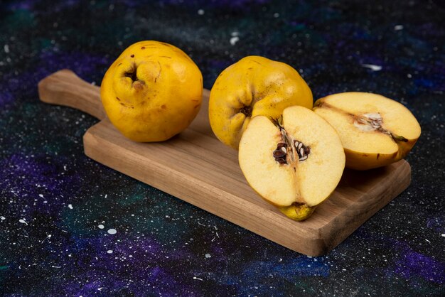 Sliced and whole fresh quince fruits on wooden board. 