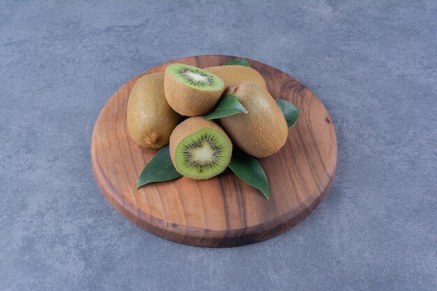 Sliced and whole kiwi fruits on board on marble table.