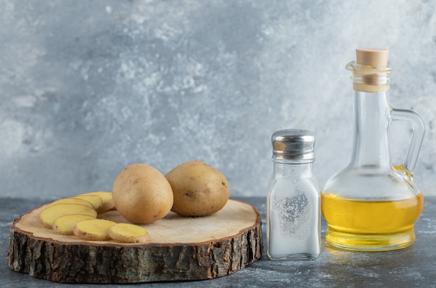 Free photo sliced and whole potatoes on wooden board with salt and oil.