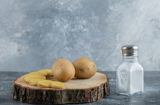 Sliced and whole potatoes on wooden board with salt.