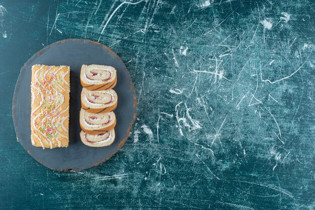 Sliced and whole roll cakes on a board, on the blue background. High quality photo