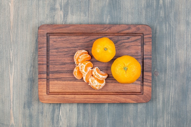 Sliced and whole tangerines on a wooden cutting board