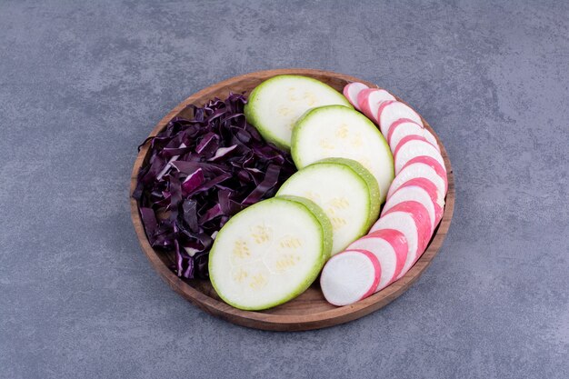 Free photo sliced zucchini, purple cabbage and pink radish on a wooden platter.