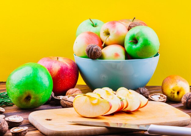 Slices of apple on chopping board with fruits and walnuts