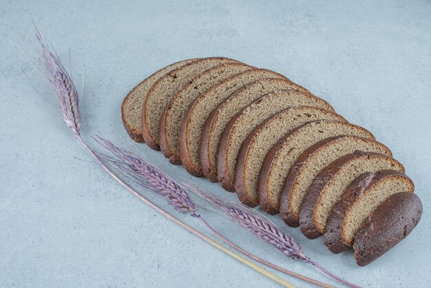 Slices of black bread on stone surface with wheat