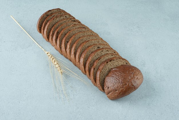 Slices of black bread on stone surface with wheat