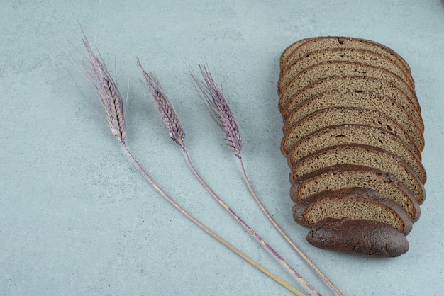 Slices of black bread on stone surface with wheat