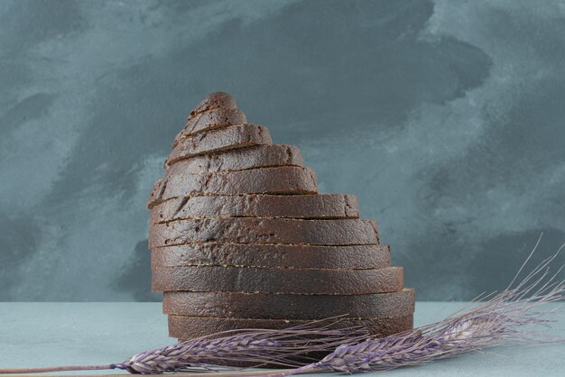 Slices of black bread on stone table with wheat