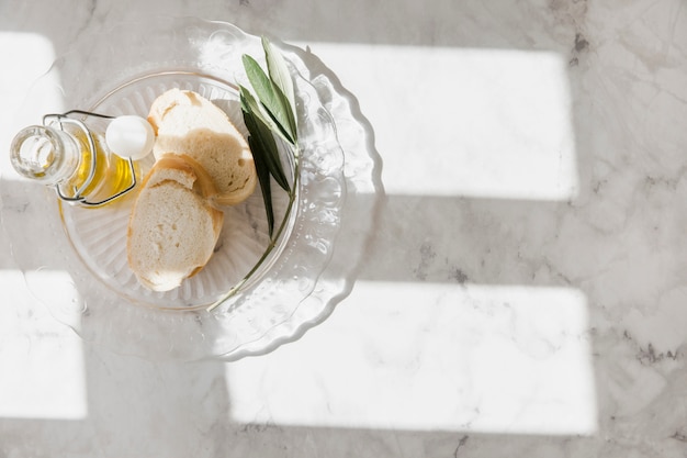 Slices of bread and olive oil bottle on glass plate over the marble backdrop