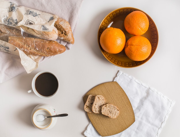 Free photo slices of bread; whole oranges; tea cup and powdered milk on white background