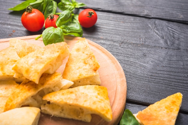 Slices of bread with basil leaves and tomatoes on wooden table