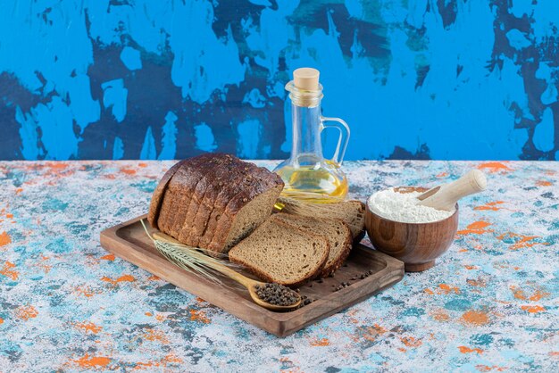 Slices of brown bread with flour and bottle of oil on wooden board.