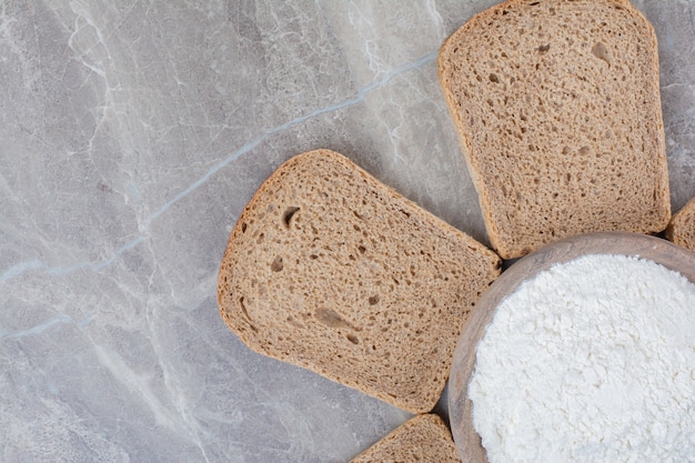 Foto gratuita fette di pane integrale con farina sulla superficie di marmo