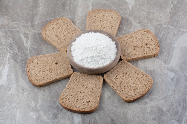 Foto gratuita fette di pane integrale con farina sulla superficie di marmo