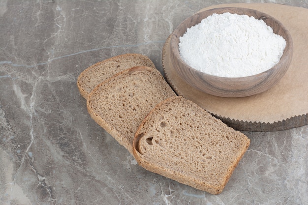 Fette di pane integrale con farina sulla superficie di marmo