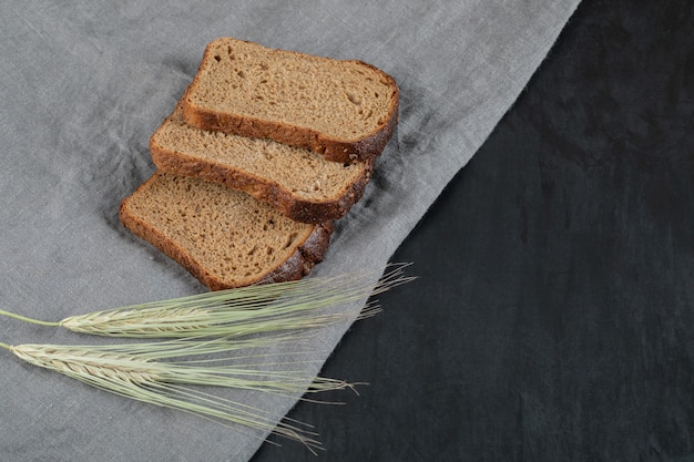 Кусочки черного хлеба с пшеницей на серой скатерти.