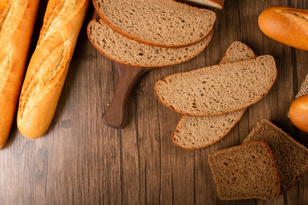 Slices of brown and white bread on kitchen board with baguette