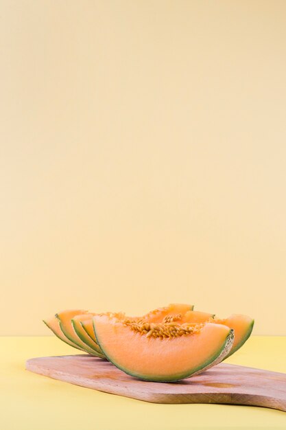Slices of cantaloupe on wooden chopping board against beige backdrop
