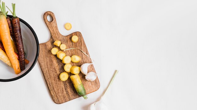 Slices of carrot and garlic cloves on chopping board over white background