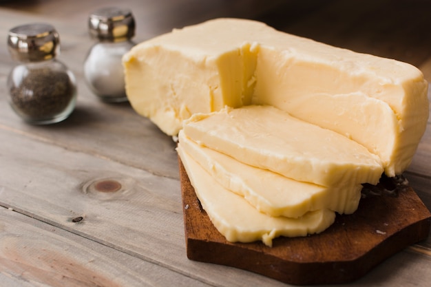 Slices of cheddar cheese on chopping board with slat and pepper shaker on table