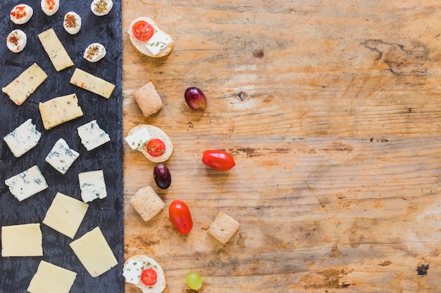 Free photo slices of cheese; tomatoes and grapes on wooden surface