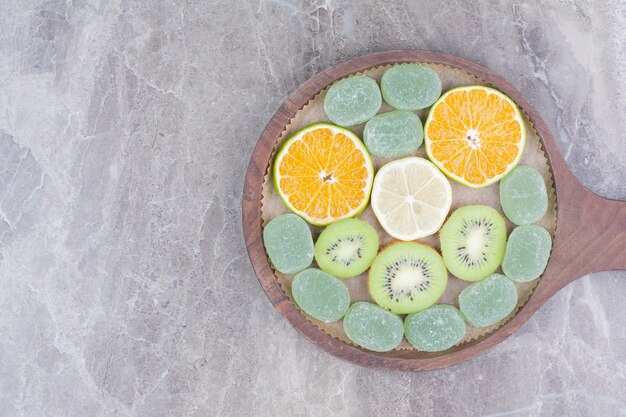 Slices of citrus fruits, kiwi and candies on wooden board. 