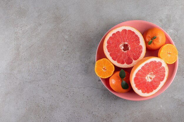 Slices of citrus orange and grapefruit fruits placed on a pink bowl