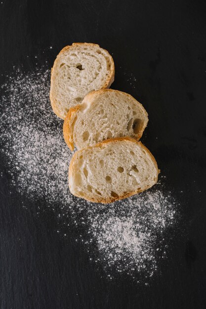 Slices of fresh breads and flour on black background