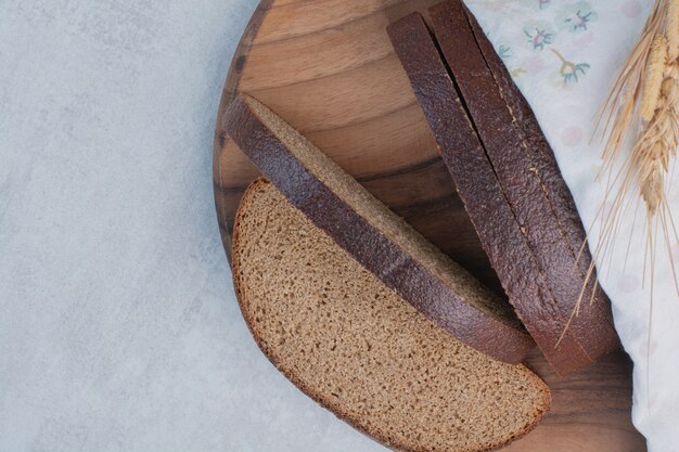Slices of fresh brown breads on wooden board .