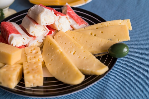 Slices of fresh cheese near snacks and pick on plate