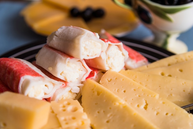 Slices of fresh cheese near tasty snacks on plate