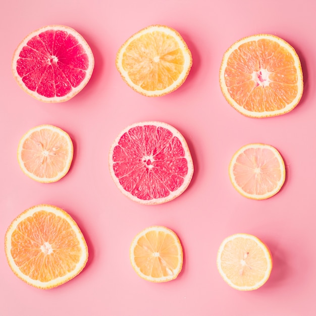 Slices of fresh citrus fruits on pink background
