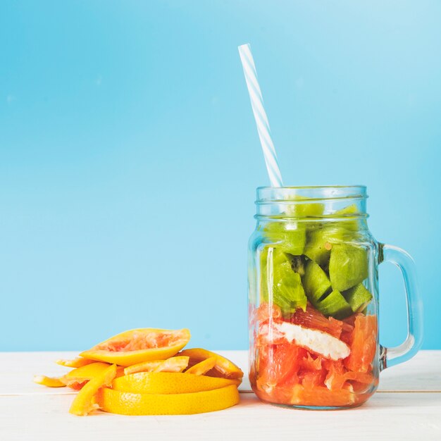 Slices of fresh fruits in jar against blue wall