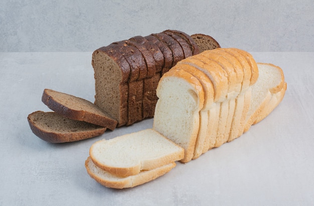 Кусочки свежего белого и черного хлеба на мраморном фоне.