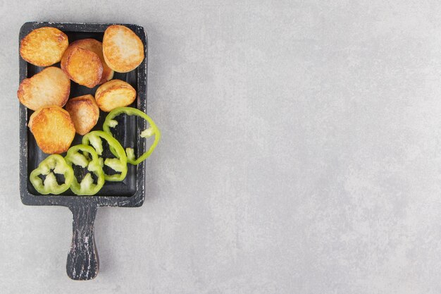 Slices of fried potatoes and peppers on black board.