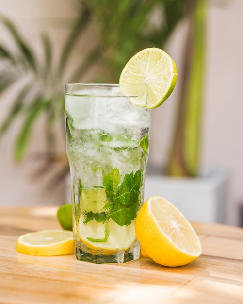 Free photo slices of fruits near glass of drink with ice and herbs on table