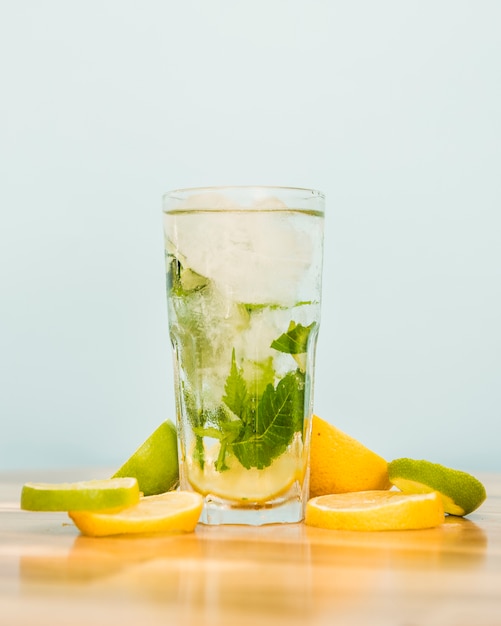 Slices of fruits near glass of drink with ice and herbs