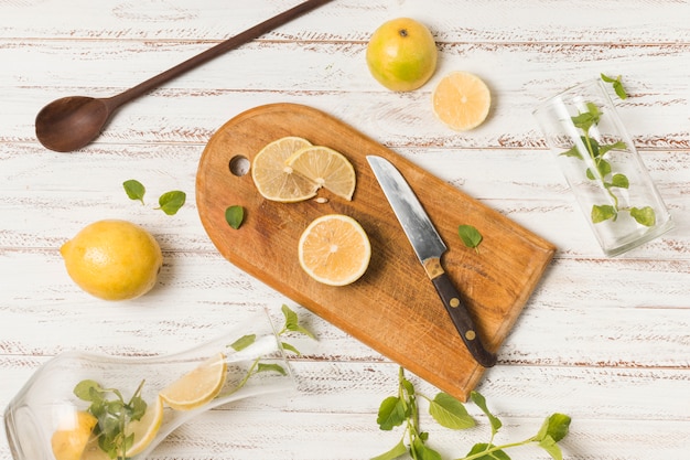 Slices of fruits near knife between herbs and glasses
