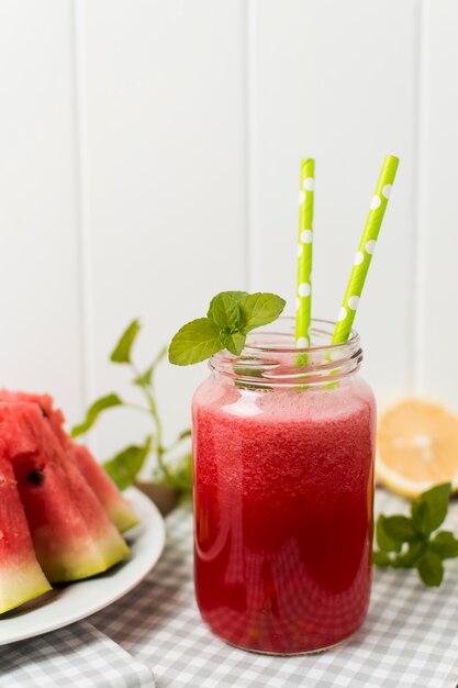 Slices of fruits on plate and glass with cocktail on napkin near plants