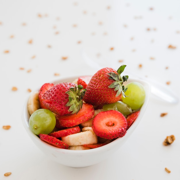 Slices of fruits in white bowl spread with oats on white backdrop