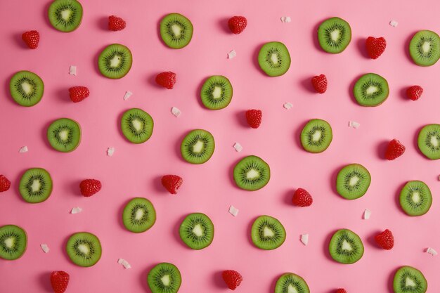 Ломтики зеленого киви, свежей малины и кокосовой стружки, изолированные на розовом фоне студии. Концепция питания питательных веществ. Композиция из сочных фруктов. Летнее время, полезные ингредиенты