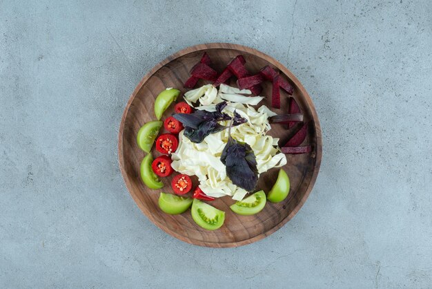 Slices of green tomato and chopped cabbage on wooden plate.