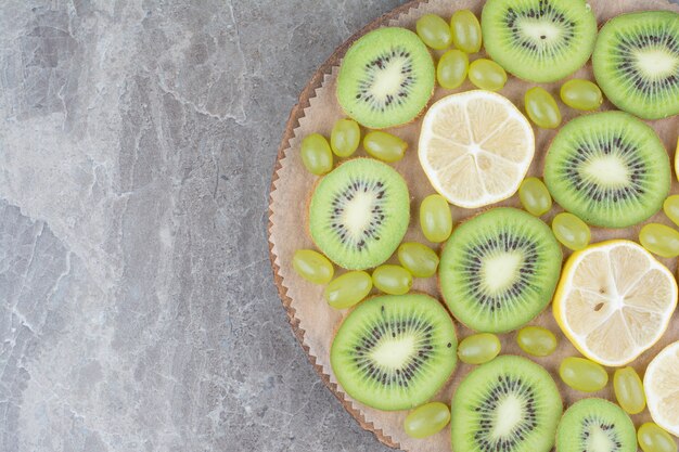 Slices of kiwi, grapes and lemon on wooden board. 