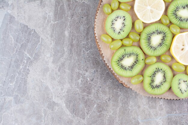 Slices of kiwi, grapes and lemon on wooden board. 