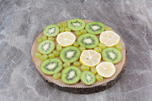 Foto gratuita fette di kiwi, uva e limone su tavola di legno.