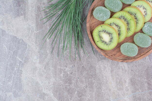 Slices of kiwi and marmalades on wooden plate with branch. 