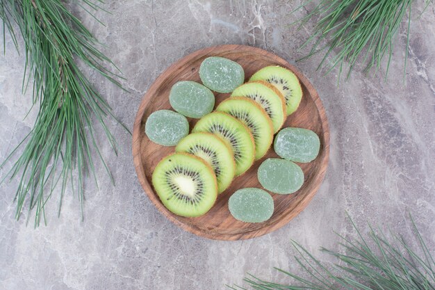 Slices of kiwi and marmalades on wooden plate with branch. 